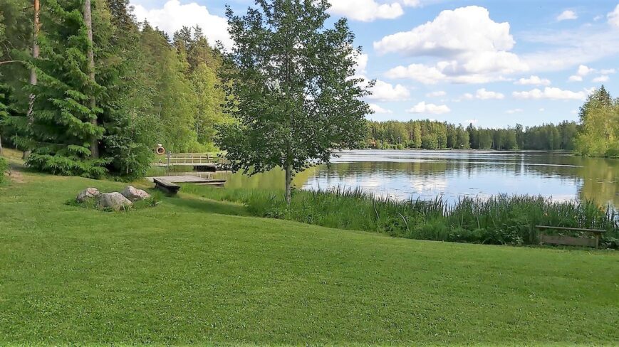 Rantanäkymä Pappisten lavalla vihreä nurmialue ja järvi taustalla.