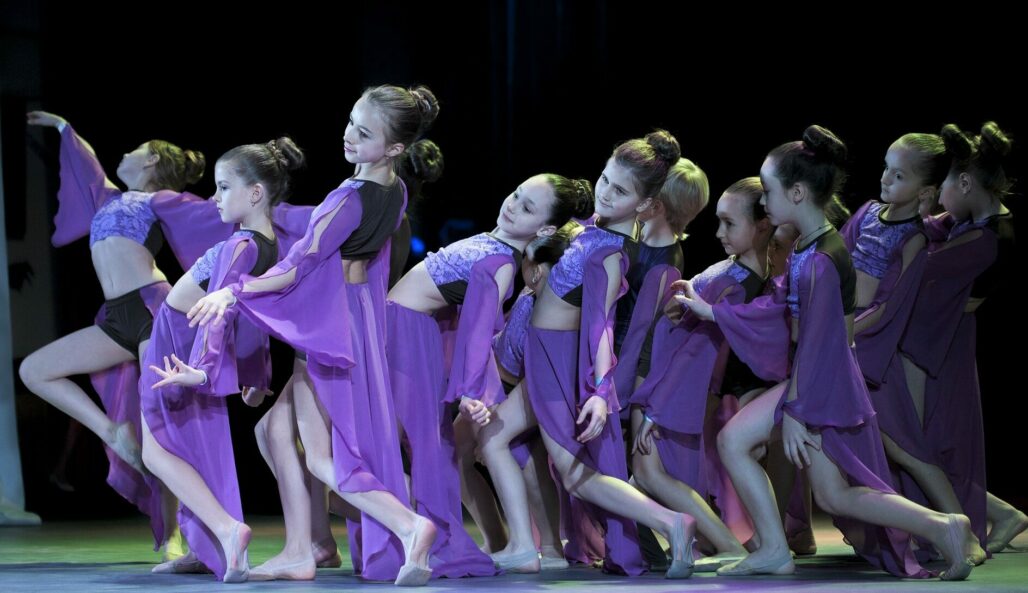 Tumman liilan värisissä puvuissa tanssivia tyttöjä.