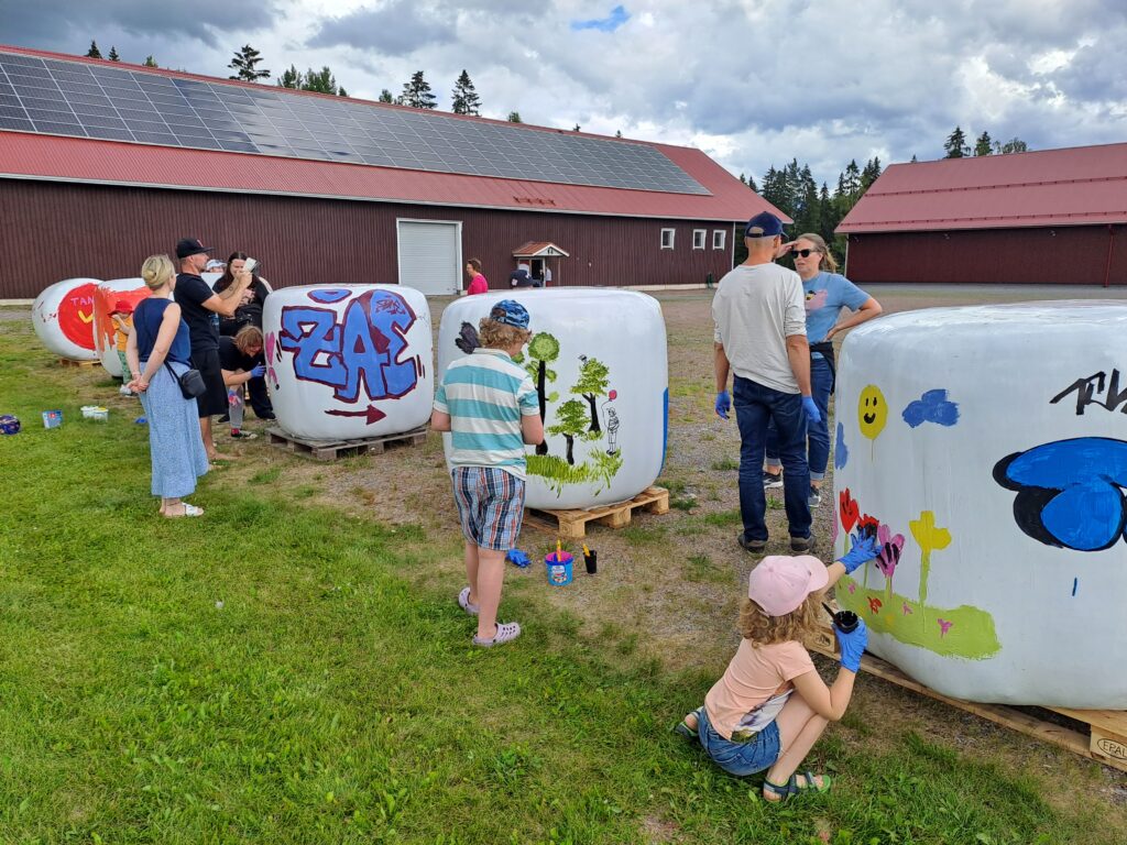 Lapsia ja aikuisia maalaamassa isoja muovitettuja heinäpaaleja.