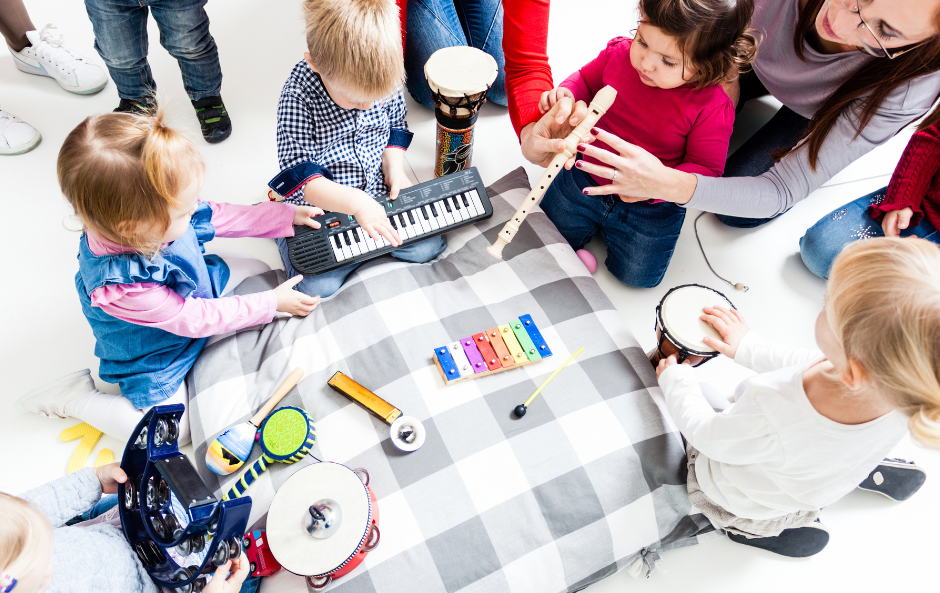 Ryhmä pieniä lapsia muskari opettajan kanssa. Lapsilla erilaisia soittimia käsisään.