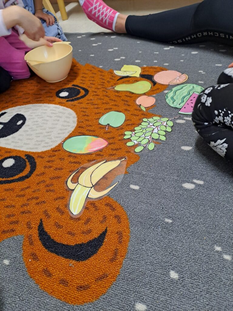 Lasten leikkihetki hedelmien kuvia lattialla maton päällä.