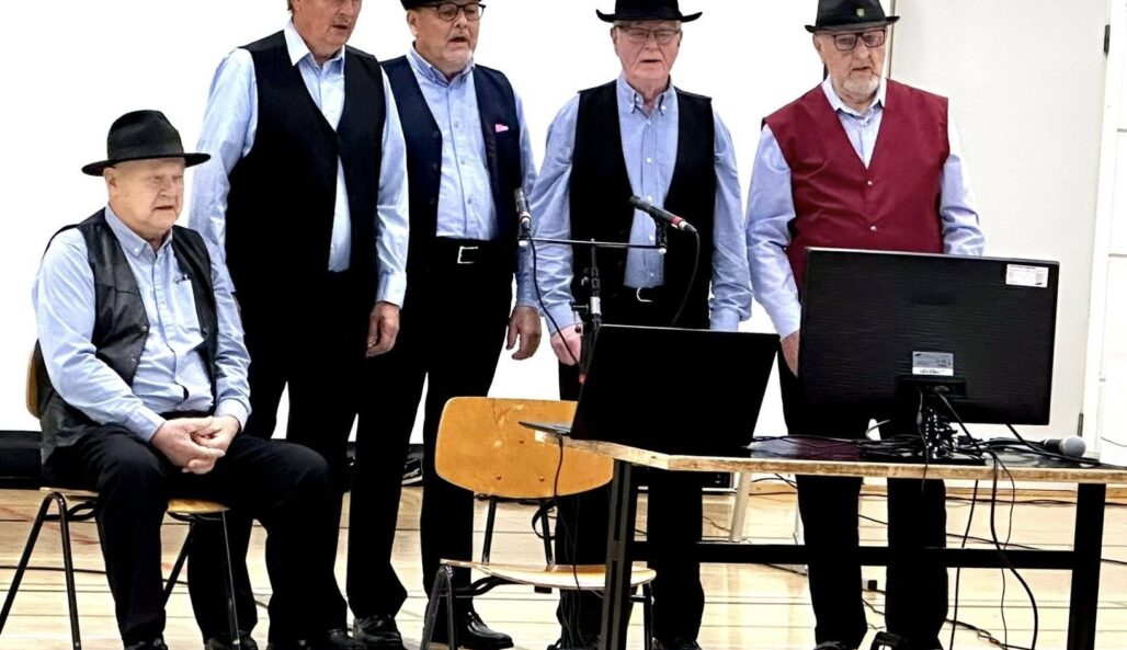 viisi miestä hatut päässä esiintyy laulaen.