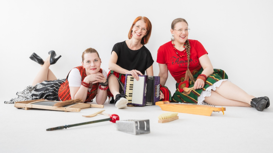 Ämmät Äänessä yhtyeen jäsenet Elsa Hietala, Iina Wahlström ja Laura Kilpiö istumassa lattialla erilaisten instrumenttien kanssa.