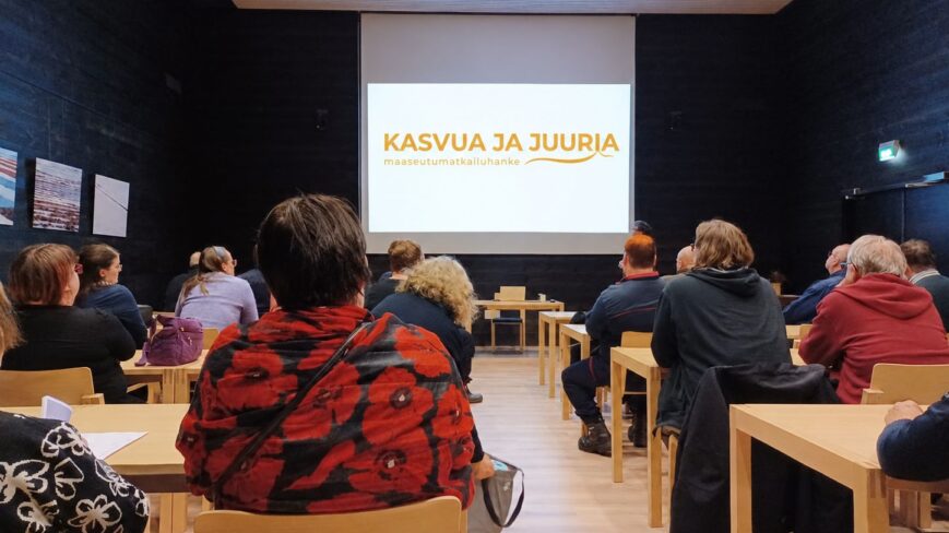 Ihmisiä istumassa pöytien ääressä kokoustilassa